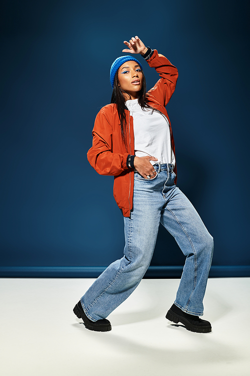 A young woman poses stylishly in her autumn outfit against a blue background.