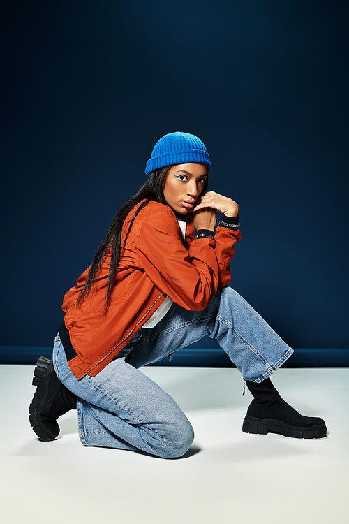 A young woman kneels in trendy autumn attire, highlighting her fashion sense and confidence.