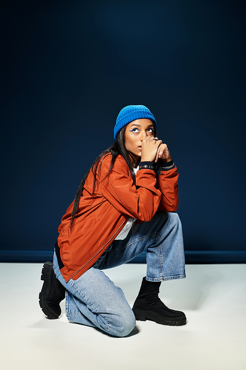 A young woman crouches, showcasing her stylish autumn outfit against a dark backdrop.