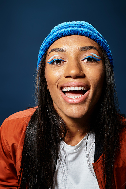 The young woman smiles brightly, showcasing her stylish warm attire against a dark backdrop.