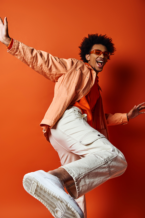 An energetic young African American man jumps in the air with arms outstretched, exuding joy and freedom against an orange backdrop.