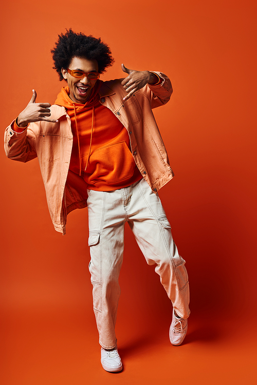 Stylish young curly man in trendy orange shirt and white pants posing emotionally on a vibrant background.