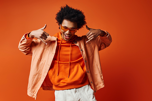 A stylish young African American man with curly hair wearing hoodie and white shorts on an orange background.