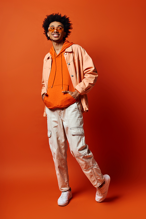 Young African American man in trendy attire and sunglasses, expressing emotions on orange background.