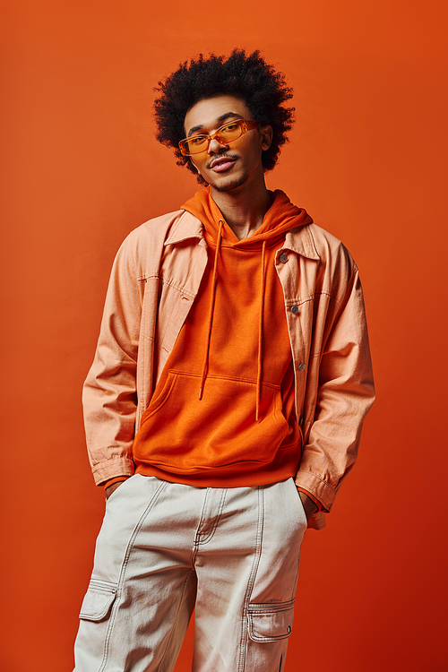 Stylish young African American man in orange hoodie and white pants, exuding confidence and emotion.