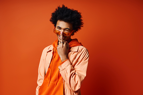 Stylish young African American man, curly hair, orange shirt, hands on face, expressing emotion, trendy background.