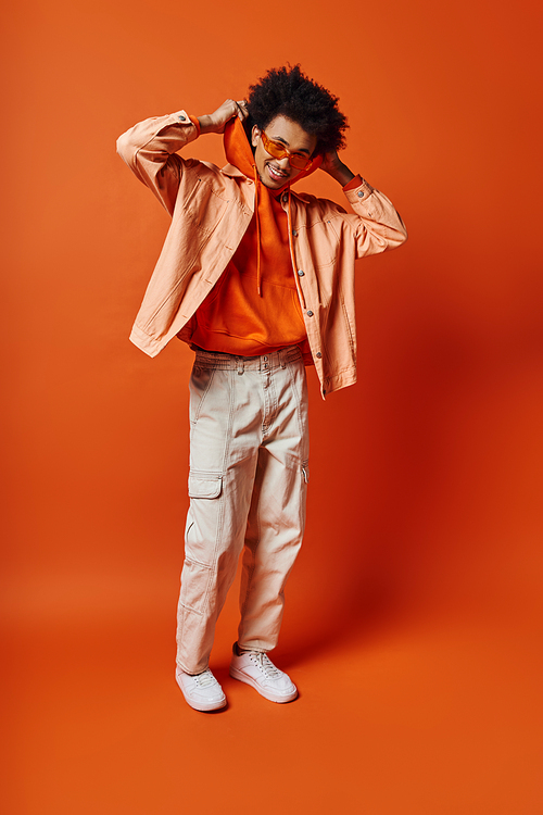 Curly African American man in trendy orange shirt and khaki pants, exuding style and charisma on a bold orange background.