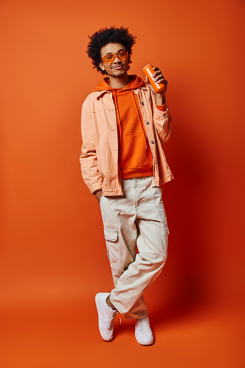 A trendy African American man with curly hair and sunglasses standing confidently against a vibrant orange background.