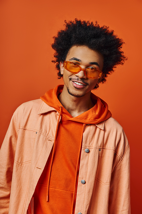 A stylish young African American man with curly hair wearing an orange shirt and jacket on an orange background, showing various emotions.