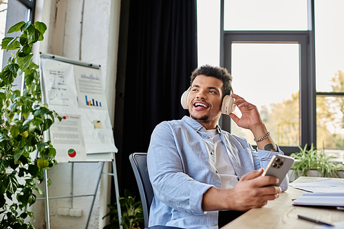 Young man listens to music and smiles, immersed in his work at a bright office space.