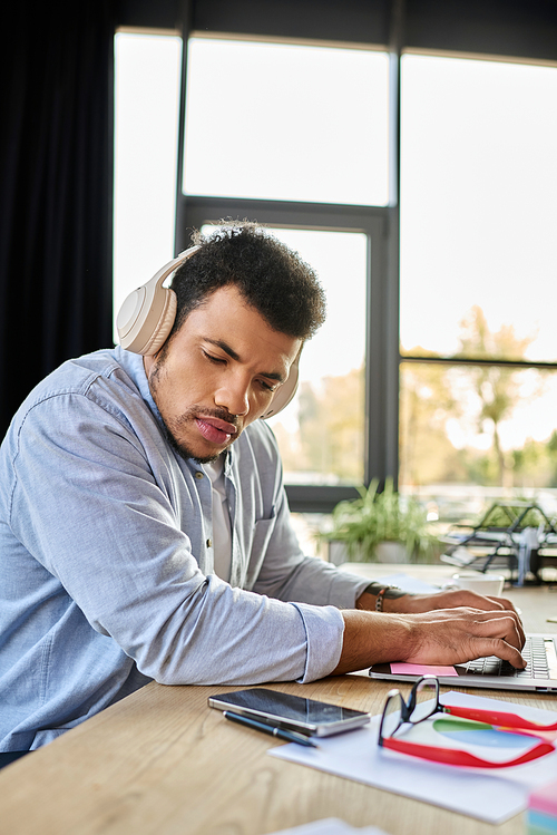 Handsome man concentrates on his laptop, surrounded by notes and devices while wearing headphones.