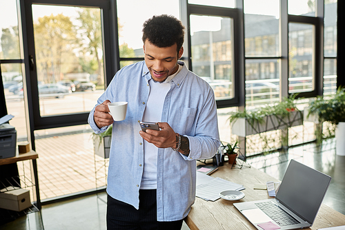 Smiling man holds a cup of coffee and checks his smartphone in a modern cafe setting.