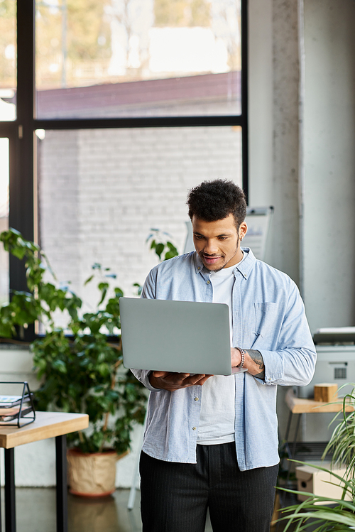 A young man with a charming smile is engaged with his laptop in a vibrant workspace.