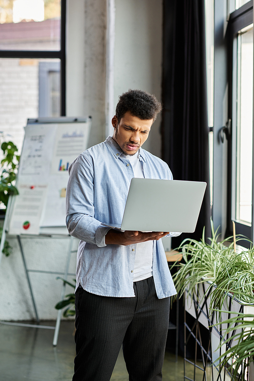 A focused man engages with his laptop in a stylish office filled with plants.