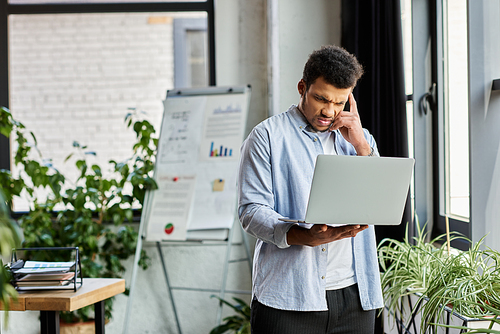 Focused individual stands in a lively workspace, engaged in a laptop call amidst greenery.