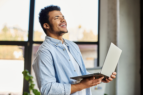 Confident man enjoying a moment of joy while using his laptop in a sunny indoor setting