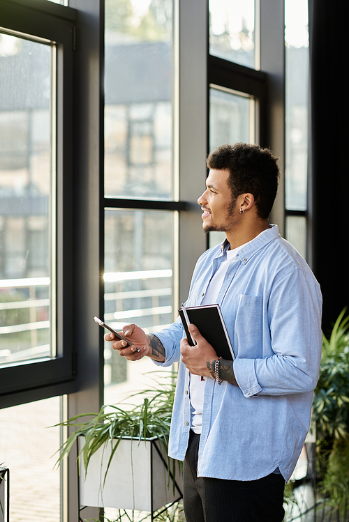 A handsome man stands by the window in bright sunlight, holding a notebook thoughtfully.