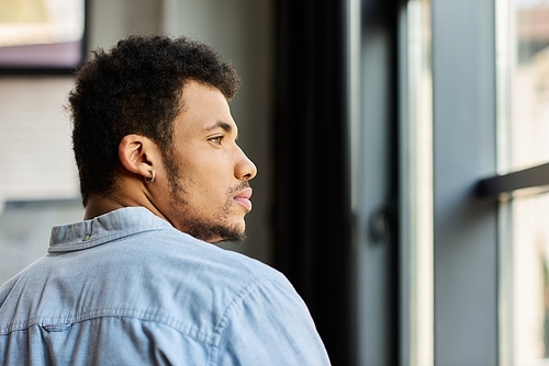 A handsome man with curly hair looks out the window, lost in thought during a serene moment.