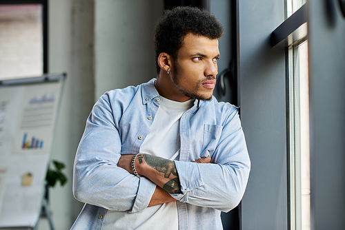 A handsome man stands thoughtfully by a window, arms crossed in a chic office setting.