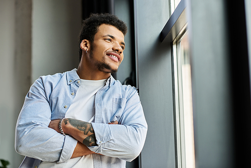 A charming man reflects joyfully while leaning against a window in a contemporary space.