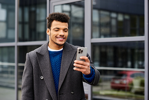 A handsome man is engaged with his smartphone, smiling in an urban setting.