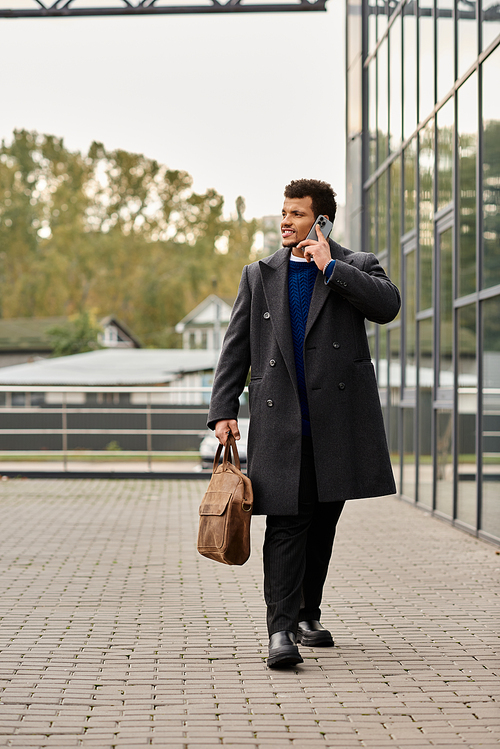 A stylish man confidently strolls by a modern building, phone to his ear.