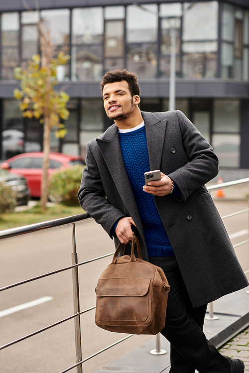 Stylishly dressed man stands by a railing, holding a phone and savoring the urban vibe.