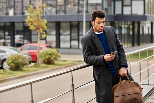 A fashionable man leans against a railing while using his smartphone in an urban setting.