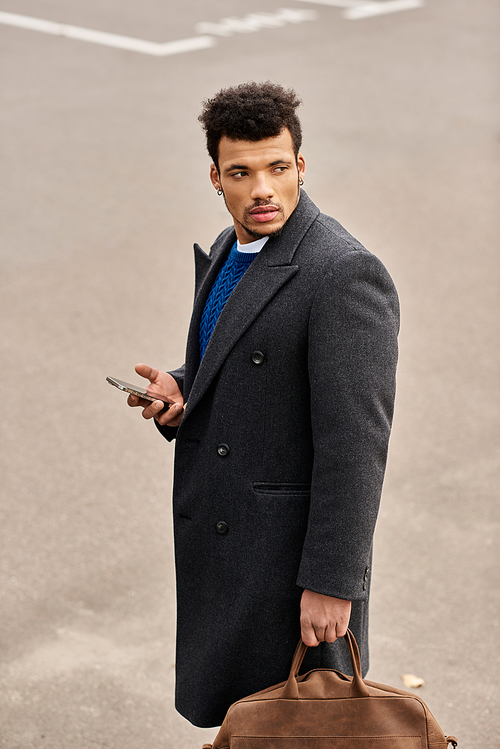 A well dressed man stands on a city street, checking his phone with a confident look.