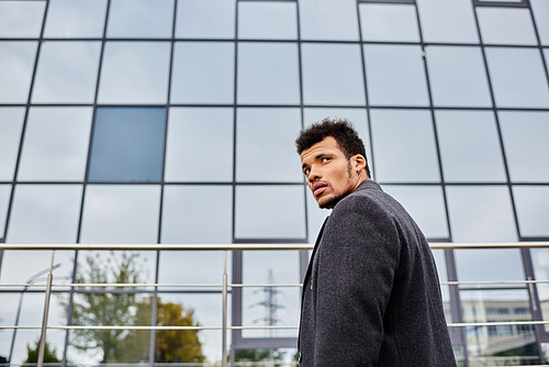 A handsome man gazes thoughtfully while standing near a sleek urban structure.