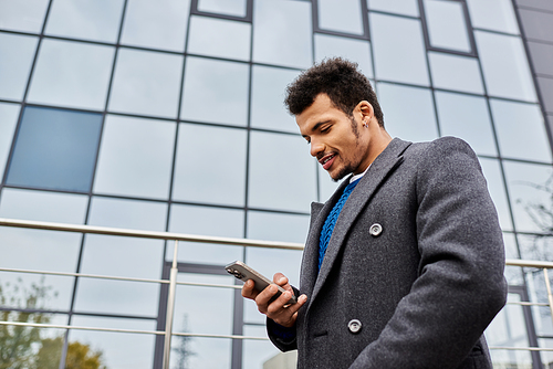 Stylish man smiles while using his smartphone outside a contemporary office building.