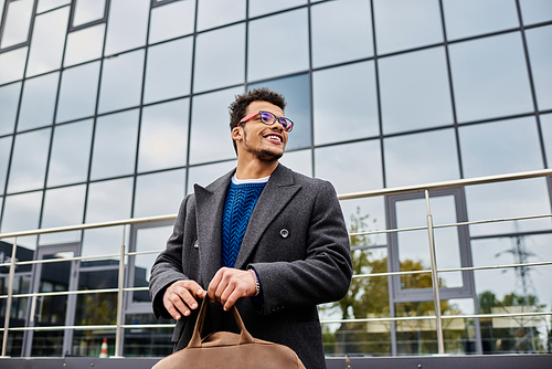 Handsome man smiles brightly while standing outside a stylish office building.