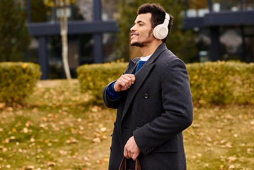 Handsome individual in a coat listens to music, embracing the autumn ambiance in the park.