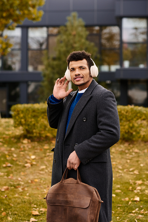 A handsome man listens to music while standing in an autumn park enjoying the scenery.