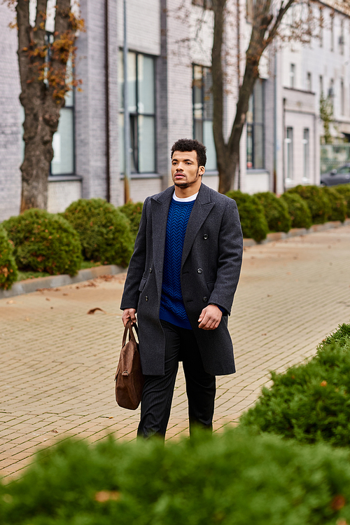 A handsome man walks confidently on a tree lined street, enjoying the crisp city air.