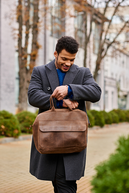 A stylish man looks cheerful while inspecting his brown bag on a pleasant day outdoors