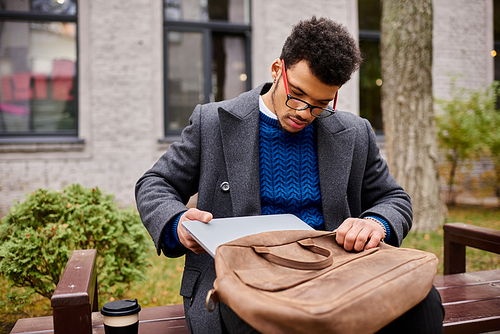 Stylish individual checks his laptop while seated on a wooden bench in a vibrant park.