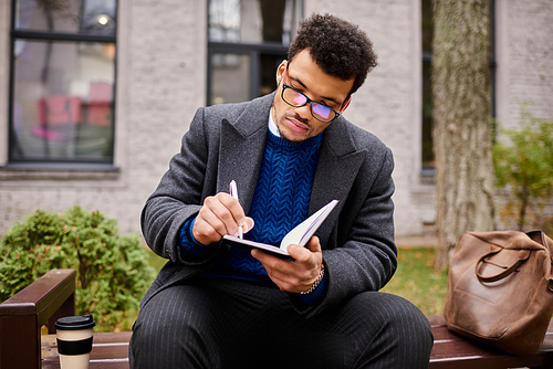 A stylish man enjoys a moment of creativity while writing in a notebook surrounded by nature