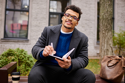 A handsome man sits comfortably writing in his notebook, surrounded by nature and warmth.