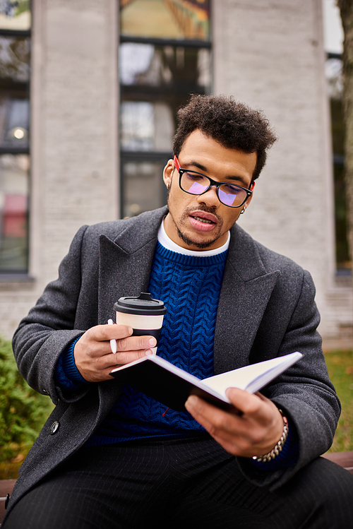 Handsome man catches up on reading while lounging outside with a warm cup of coffee.