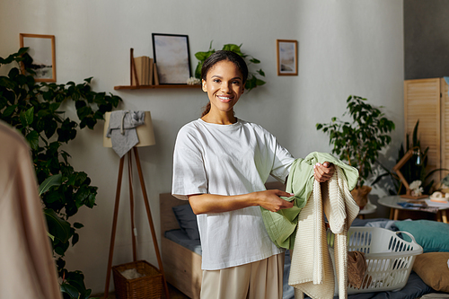 In a stylish modern apartment, a young woman cheerfully organizes her cleaning tasks while smiling.