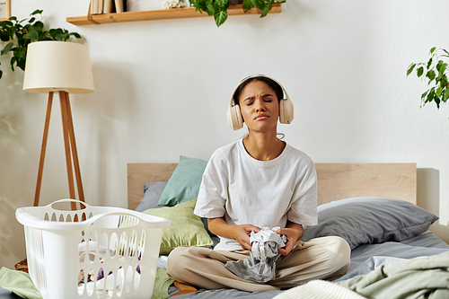 A young African American woman cleans her apartment, listening to music with joy.