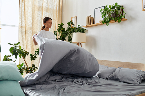 A young African American woman tidies her bedroom, fluffing pillows and making the bed.