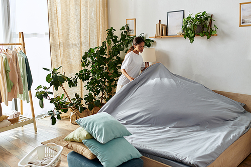 A young african american woman is making her bed while cleaning her stylish apartment.