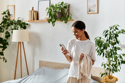 A young African American woman smiles, checking her phone and holding laundry in a chic home.