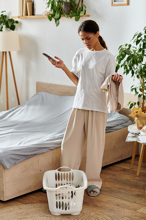 A young African American woman multitasks while cleaning, balancing chores and her phone.