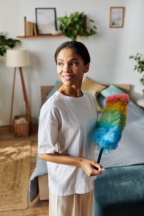 In a bright apartment, a young African American woman joyfully dusts while cleaning her home.