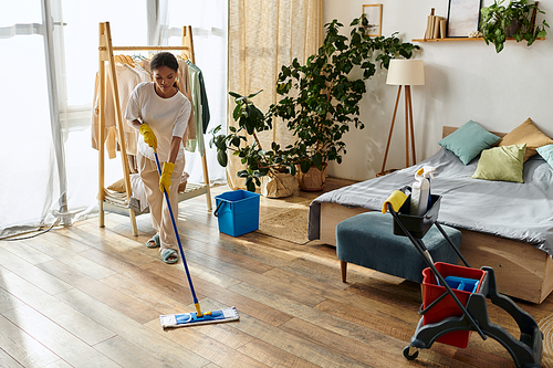 A young African American woman tidies her home while cleaning the wooden floor in her apartment.