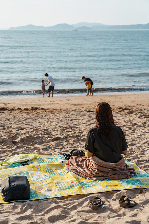 해변 모래사장에 돗자리를 깔고 휴식을 즐기는 여자의 뒷모습
