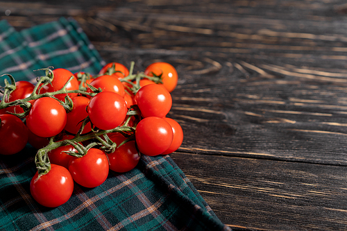 Cherry tomatoes in the checkered cloth serviette on the dark wooden table. Juicy ripe vegetables on a black background. Healthy eating. vegetarian food
